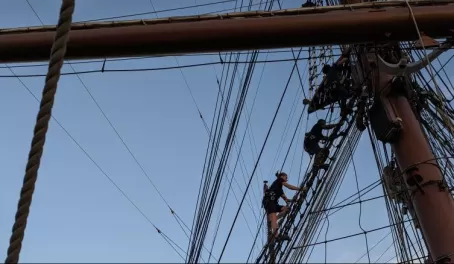 Sailors climbing to the mast of the Sea Cloud II to hoist the sails