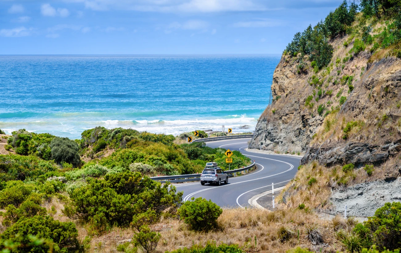 Beautiful view of the ocean, cliffs and the road winding along the coast. A car going on a road trip holiday.