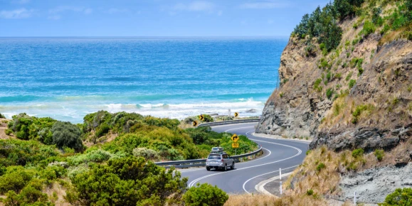 Beautiful view of the ocean, cliffs and the road winding along the coast. A car going on a road trip holiday.