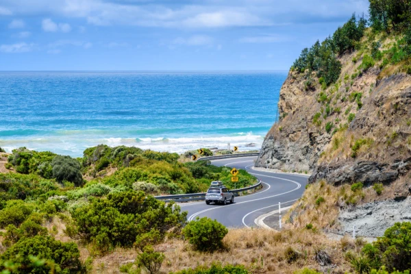 Beautiful view of the ocean, cliffs and the road winding along the coast. A car going on a road trip holiday.