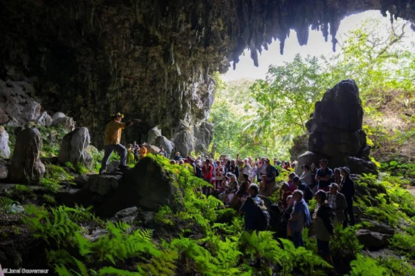 Tourists discover natural rock formations and tropical foliage inside a sea cave on Rurutu island during an excursion