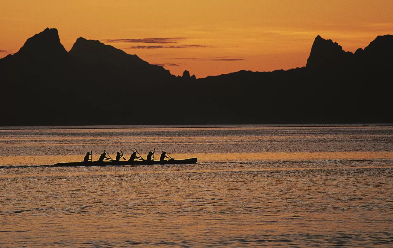 Locals paddle a traditional canoe at sunset